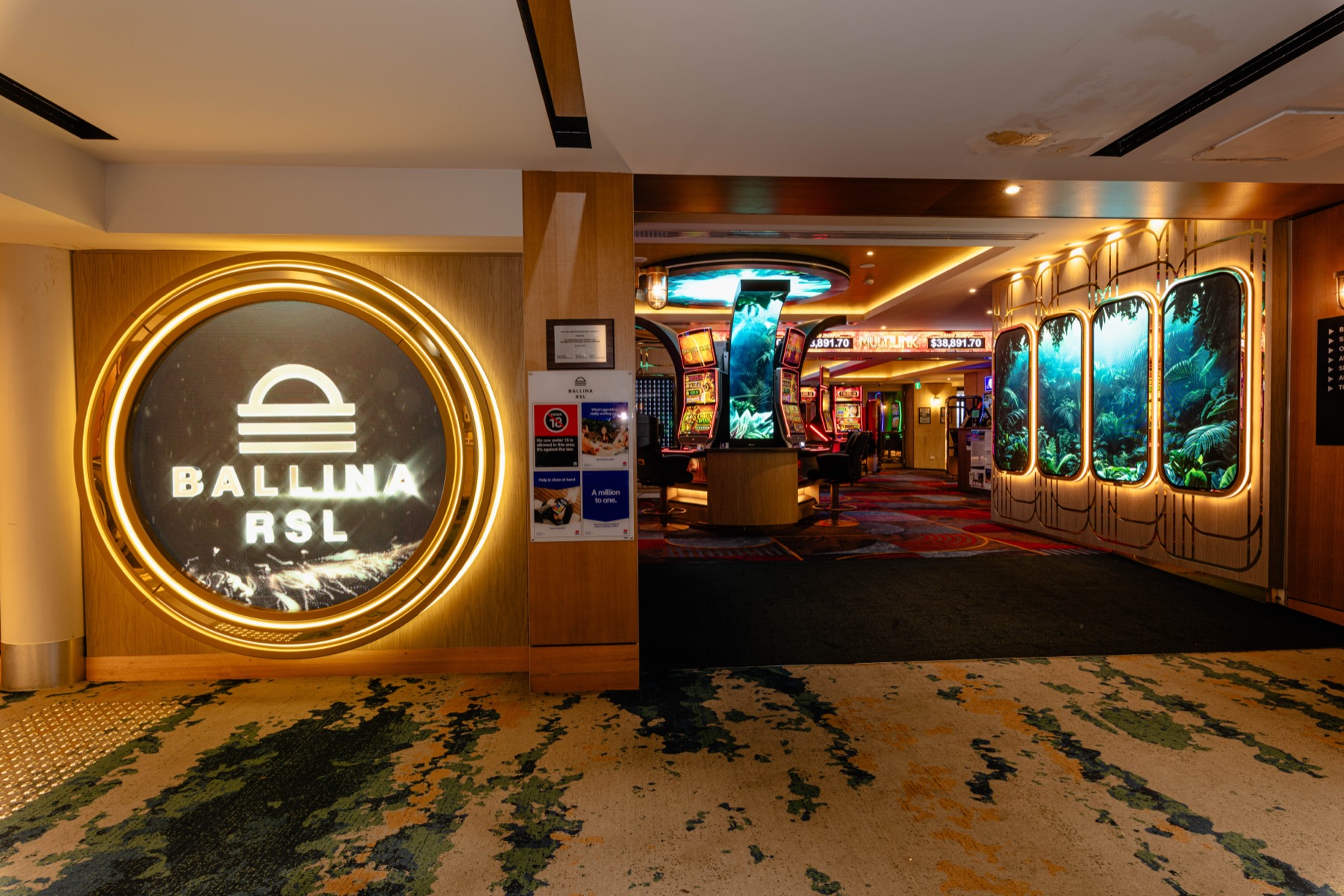 The Ballina RSL entrance: the club's sign on a round LED ring, and beyond it the gaming floor with rainforest panels glowing along the wall