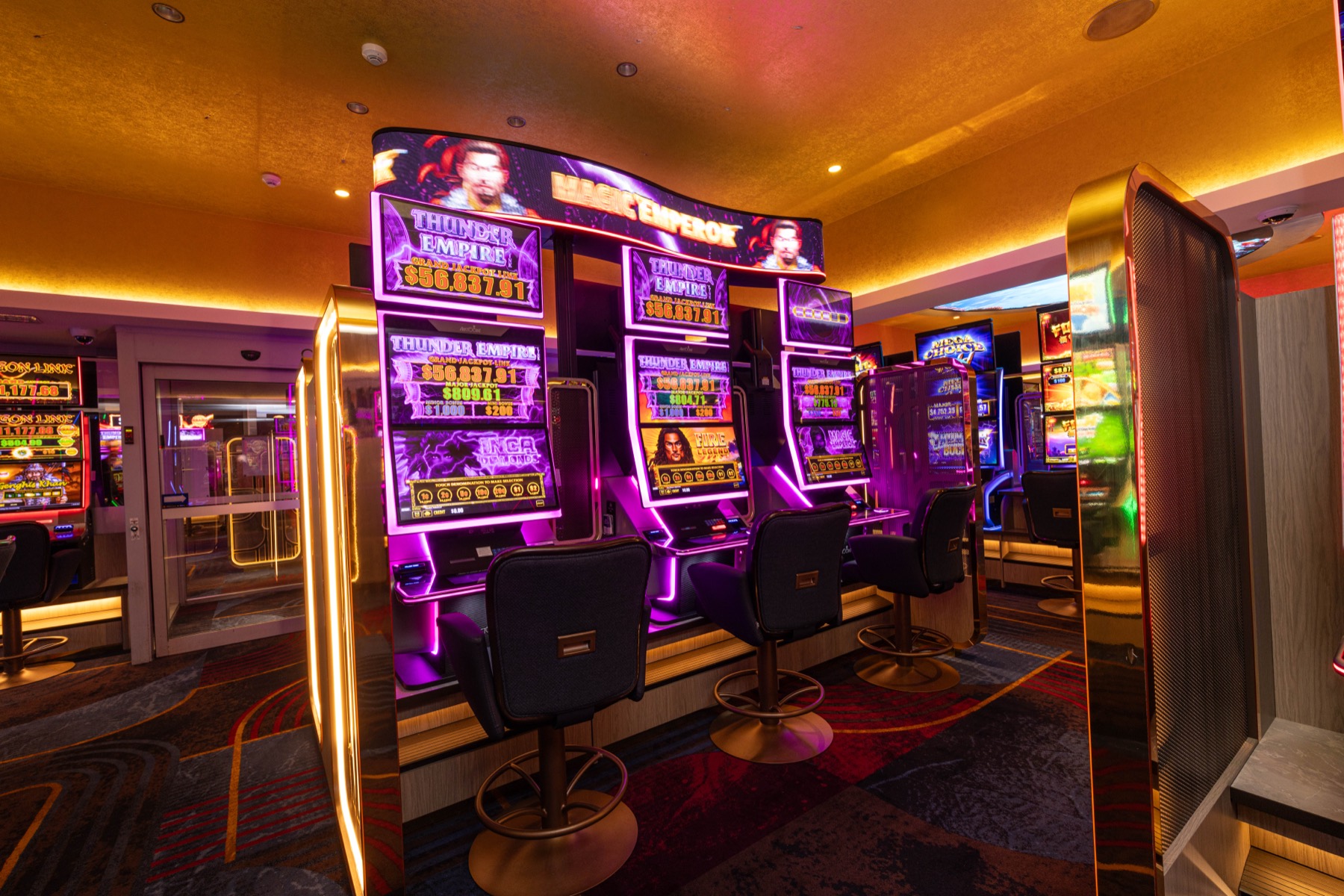 A bank of machines under a curved LED jackpot sign, edge-lit in purple