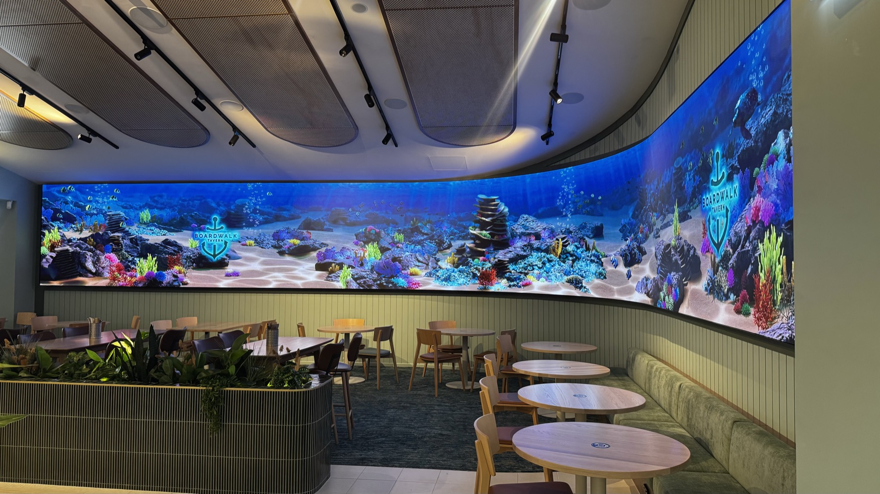 The bistro with the curved LED ribbon running the length of the wall, a coral reef scene on it, tables and planters below