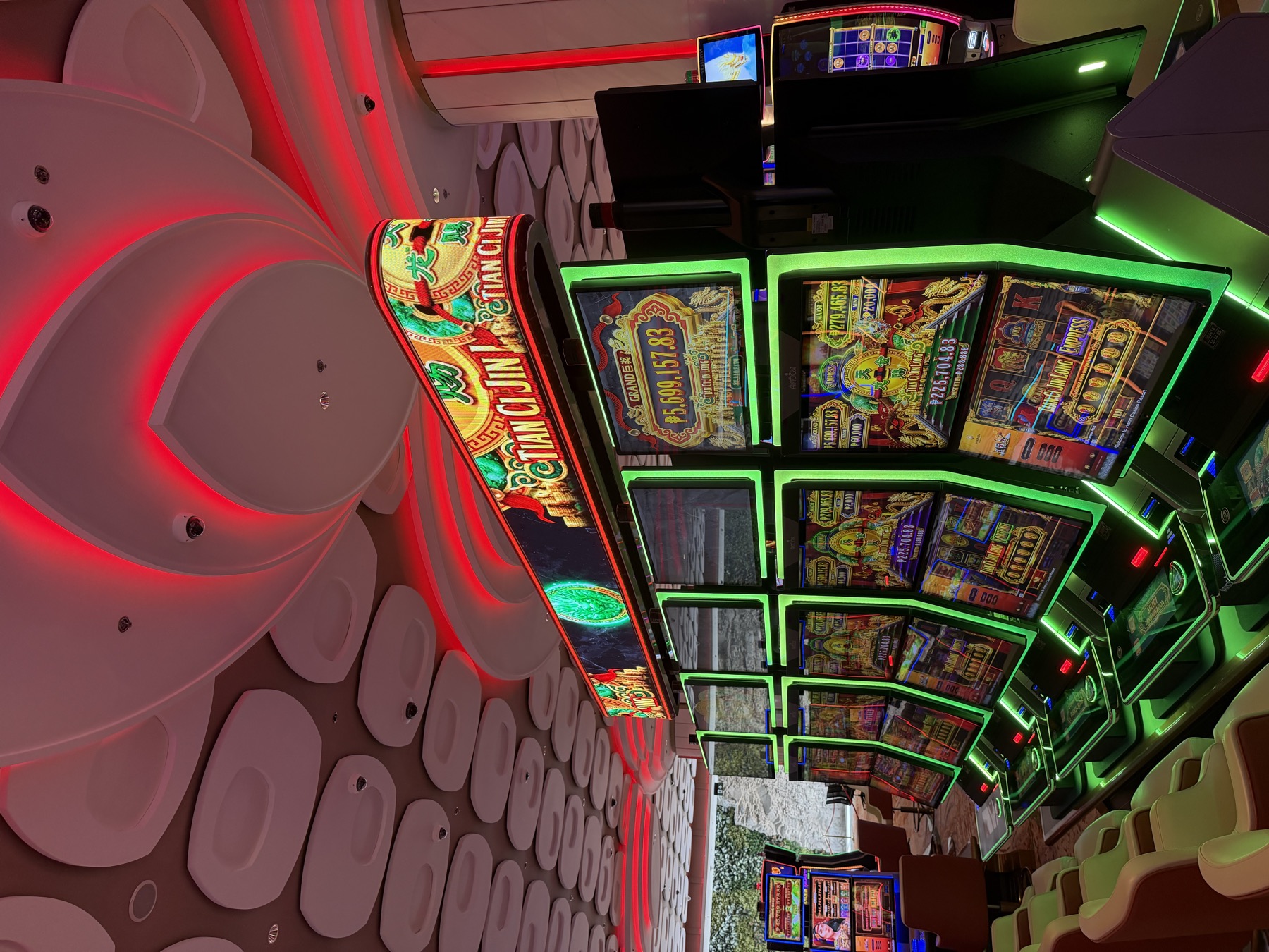A curved LED jackpot sign glowing green and gold over a bank, red light washing the sculpted ceiling above
