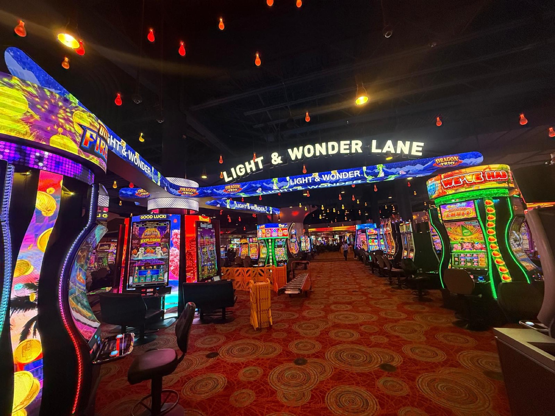 Light & Wonder Lane from the floor: a lit sign overhead, a curved LED banner running the lane, machines either side
