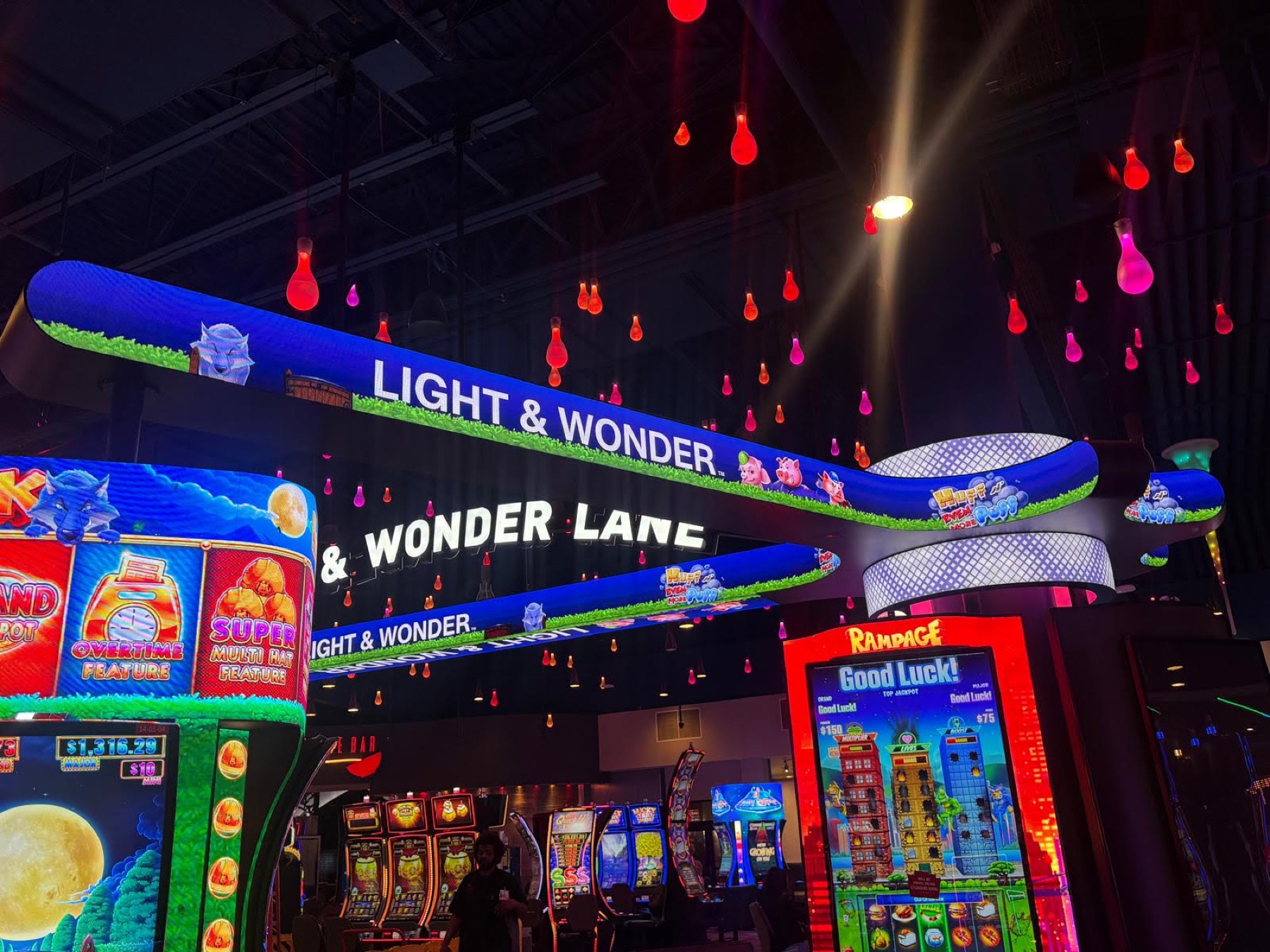 The curved LED banner from below, characters running along it under hanging coloured lamps
