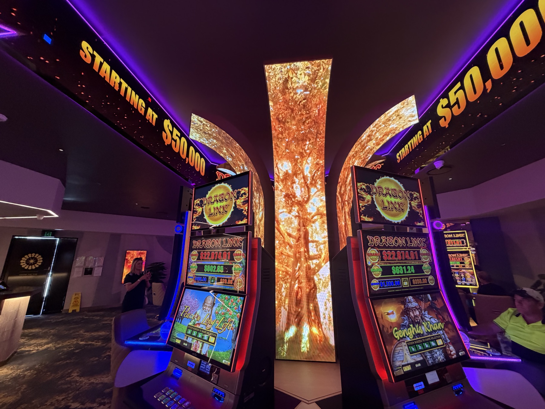 A curved LED column showing a golden tree, its branches continuing onto curved LED panels overhead, machines either side