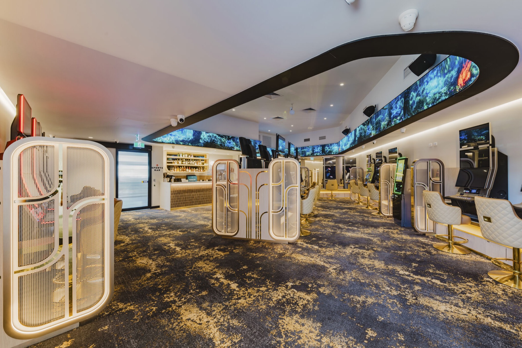 The gaming room from the entrance: an LED ribbon curving round the ceiling bulkhead with a rainforest scene on it, gold mesh screens and quilted chairs below